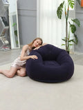 Person leaning on a dark blue inflatable lazy sofa beside a plant