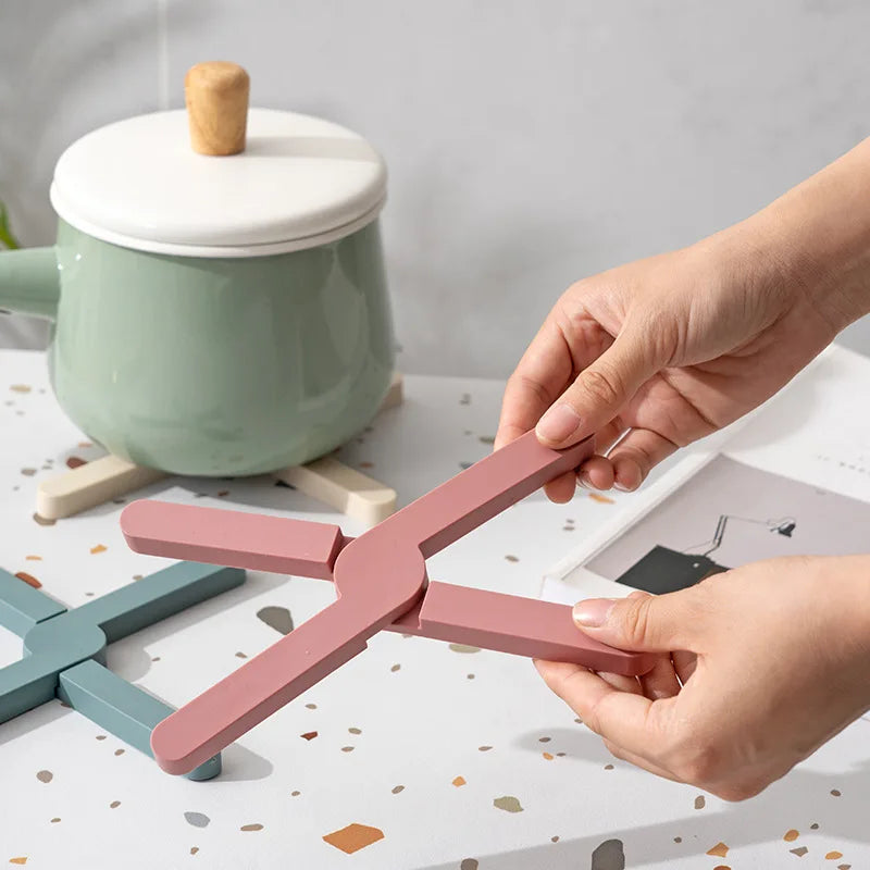 Hands unfolding a cross-shaped silicone pot mat on a table