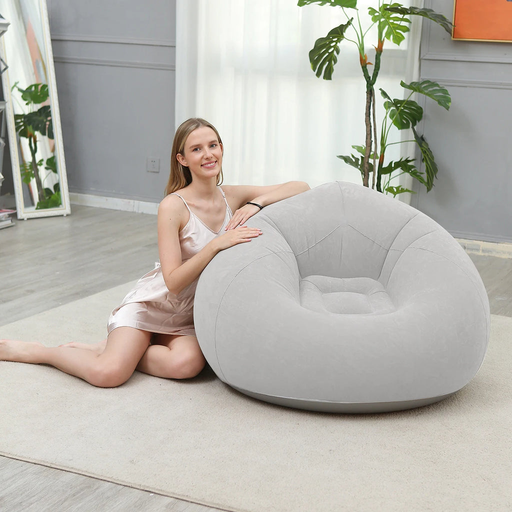 Woman sitting beside a light gray inflatable lazy sofa on a rug